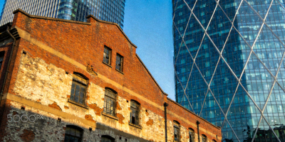 新旧建筑对比强烈的城市街区，一侧是红砖老厂房，另一侧是玻璃幕墙现代大厦