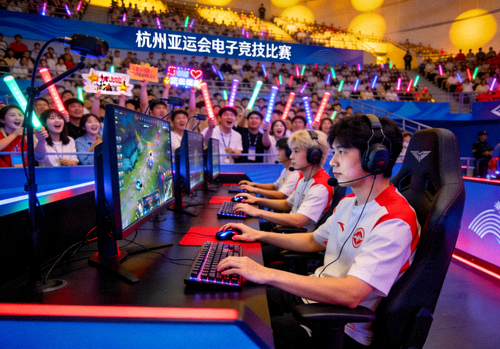 杭州亚运会电子竞技项目比赛现场，选手全神贯注操作，观众席座无虚席的热烈场景